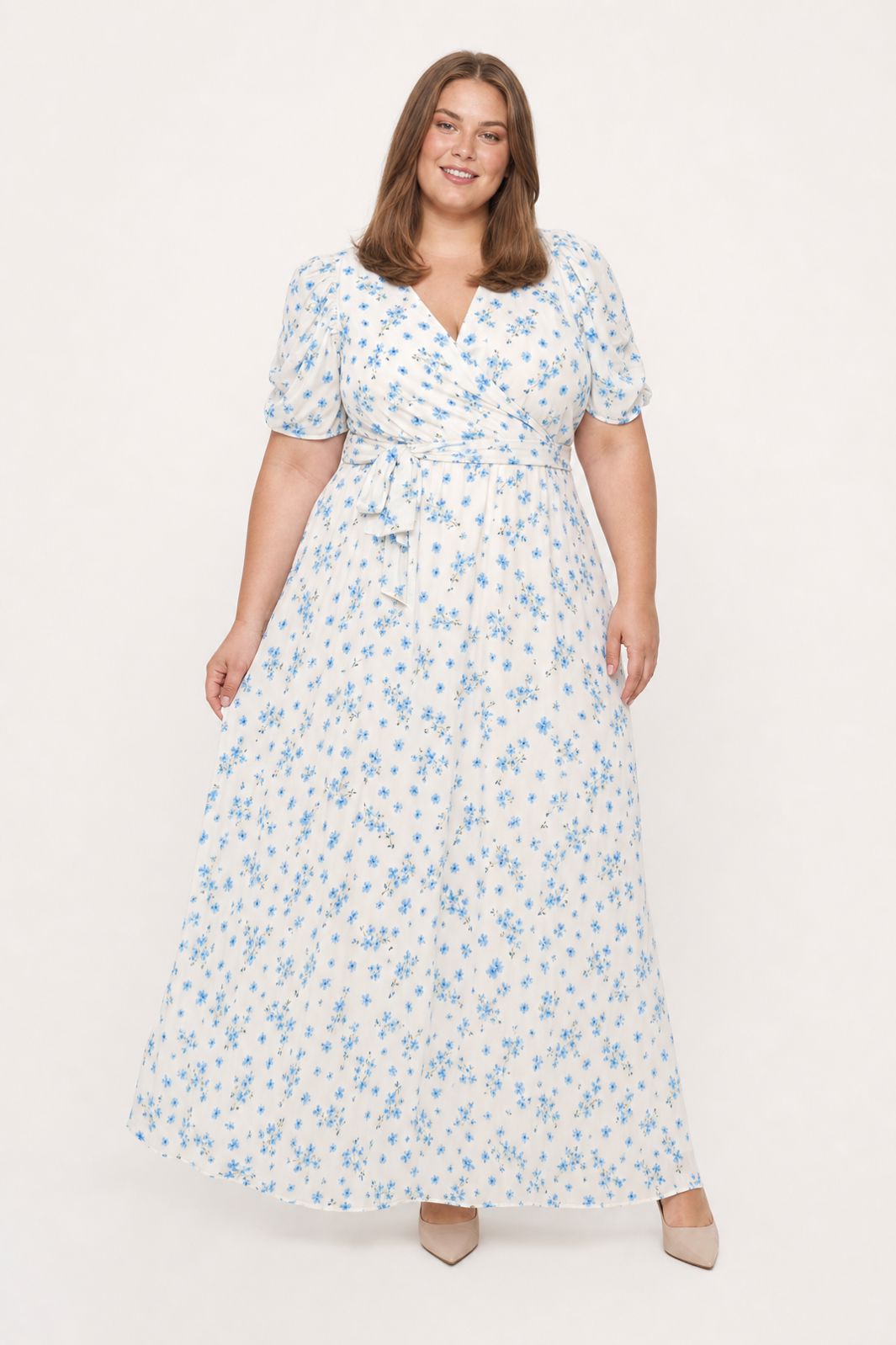 Plus-size kvinde i en lang hvid maxikjole med blåt blomsterprint mod en hvid baggrund.