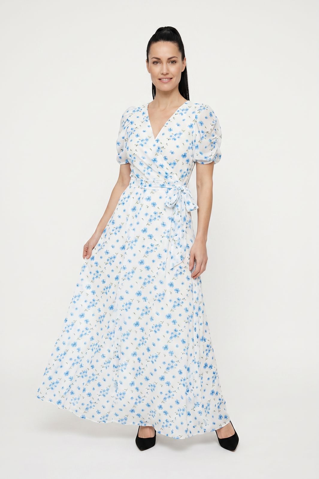 Kvinde i hvid maxi-kjole med blåt blomsterprint og korte pufærmer på hvid baggrund.