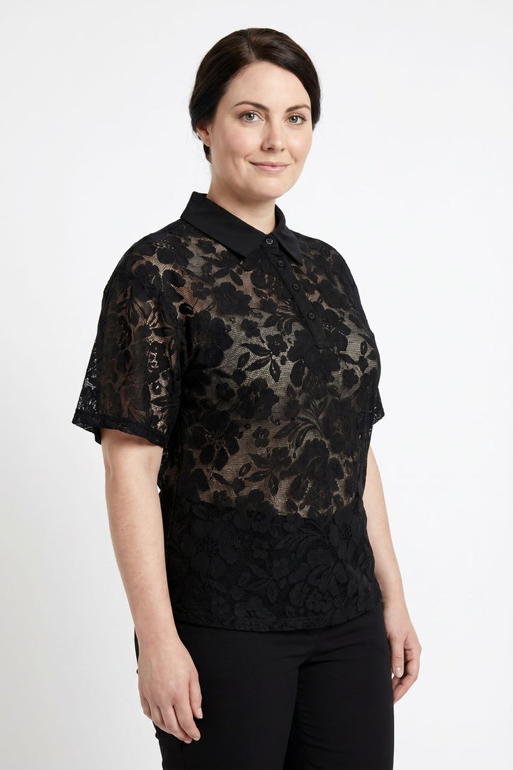 Kvinde iført en sort blomstret blonde-poloshirt og sorte bukser mod en hvid baggrund.